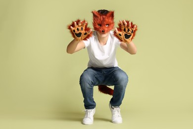 Photo of Quadrobics. Boy wearing fox mask, gloves and tail on pale olive background