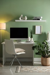 Home office. Comfortable workplace with desk, computer and lamp near light green wall in room