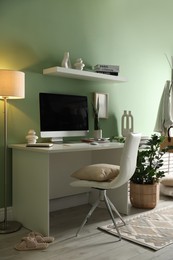 Home office. Comfortable workplace with desk, computer and lamp near light green wall in room