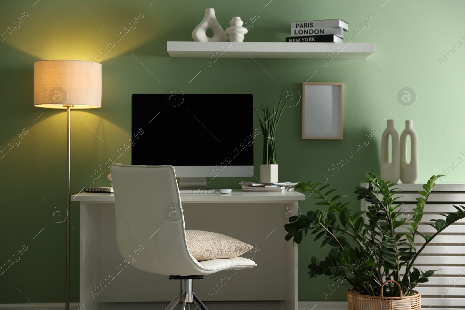 Photo of Home office. Comfortable workplace with desk, computer and lamp near light green wall in room