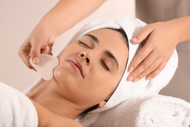 Photo of Young woman receiving facial massage with gua sha tool in spa salon