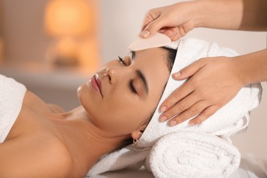 Photo of Young woman receiving facial massage with gua sha tool in spa salon