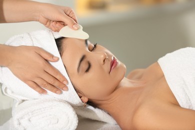 Photo of Young woman receiving facial massage with gua sha tool in spa salon