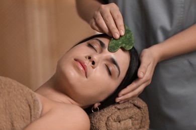 Photo of Young woman receiving facial massage with gua sha tool in spa salon