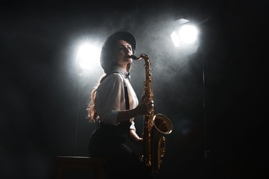 Professional musician playing saxophone on dark background with lights and smoke