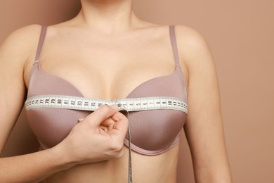 Photo of Woman in beautiful bra measuring breast circumference on beige background, closeup