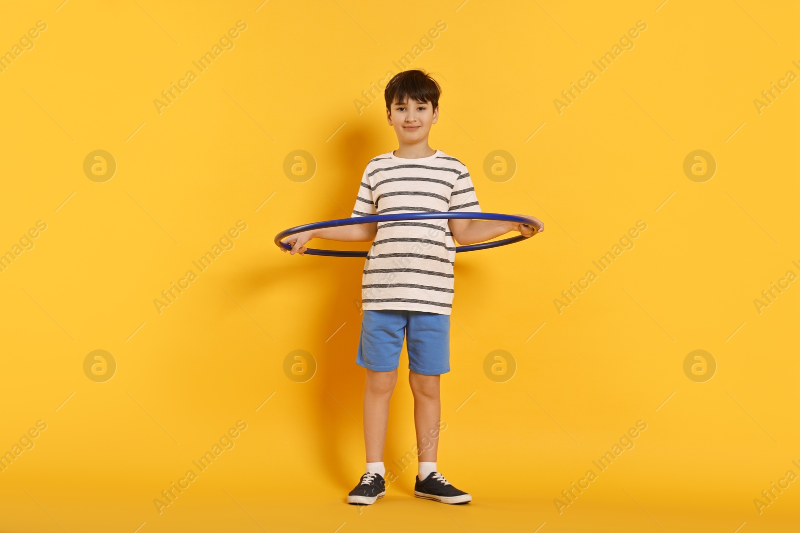 Photo of Boy exercising with hula hoop on yellow background