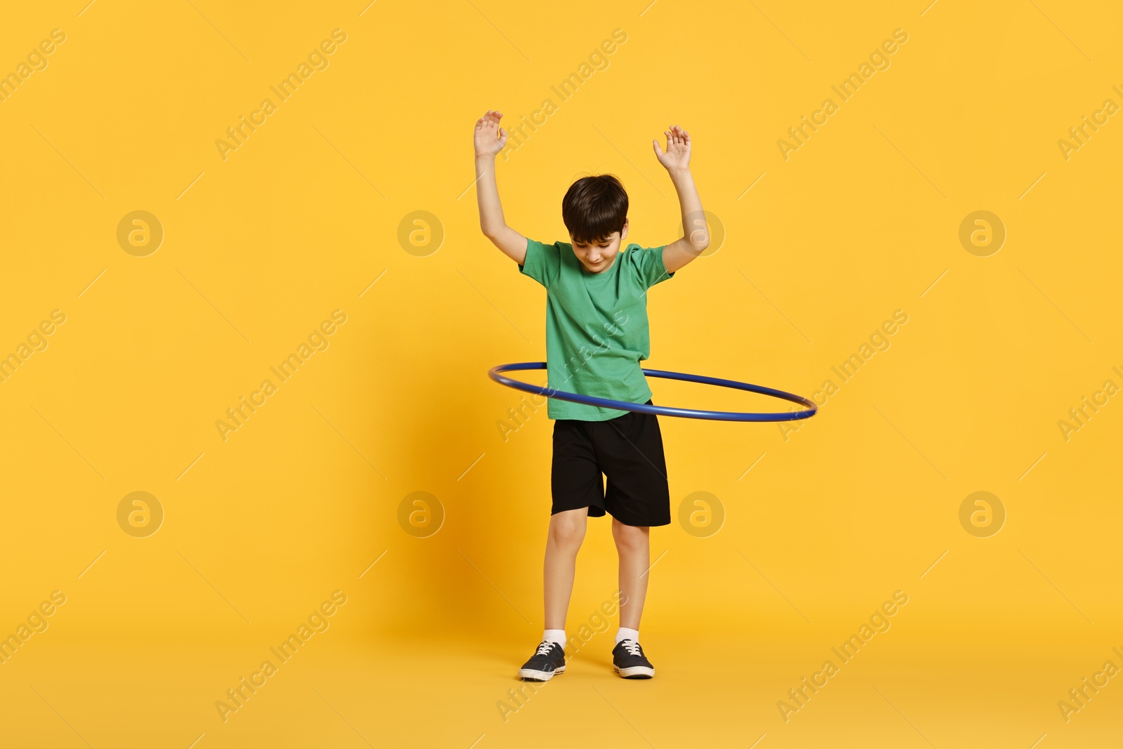 Photo of Boy exercising with hula hoop on yellow background