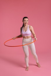 Smiling woman training with hula hoop on pink background