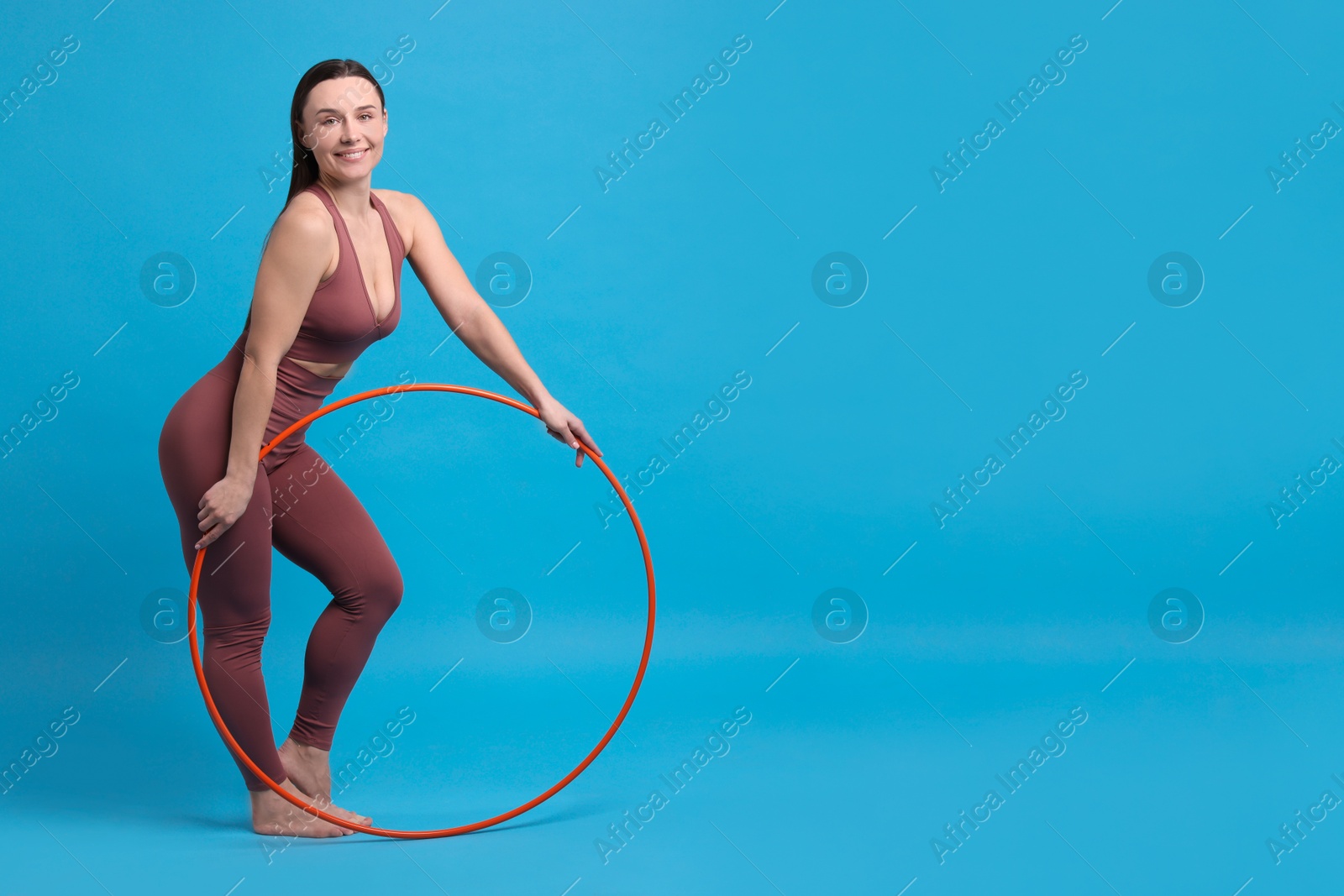 Photo of Smiling woman with hula hoop on light blue background. Space for text