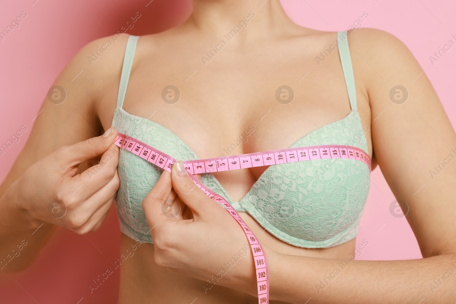 Photo of Woman in beautiful bra measuring breast circumference on pink background, closeup