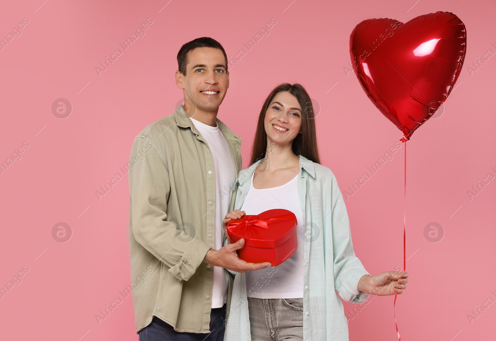 Photo of Lovely couple with heart shaped balloon and gift box on pink background. Valentine's day celebration