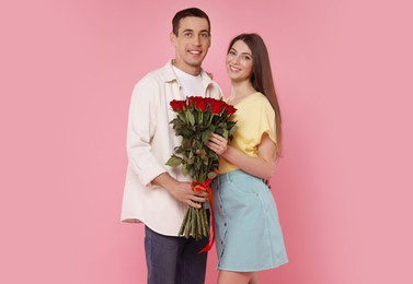 Photo of Lovely couple with bouquet of red roses on pink background. Valentine's day celebration