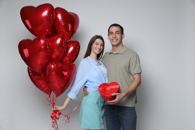 Photo of Lovely couple with heart shaped balloons and gift box on light background. Valentine's day celebration