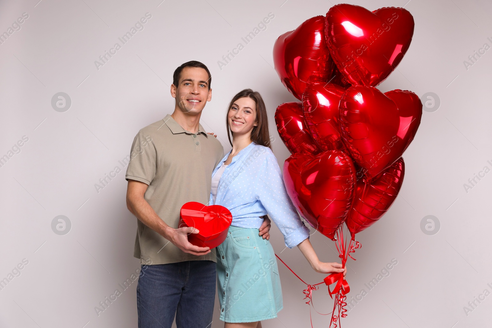 Photo of Lovely couple with heart shaped balloons and gift box on light background. Valentine's day celebration