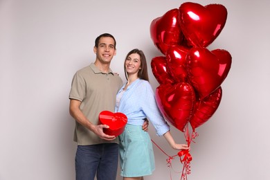 Lovely couple with heart shaped balloons and gift box on light background. Valentine's day celebration