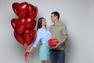 Lovely couple with heart shaped balloons and gift box on light background. Valentine's day celebration