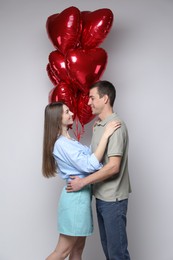 Photo of Lovely couple with heart shaped balloons on light background. Valentine's day celebration