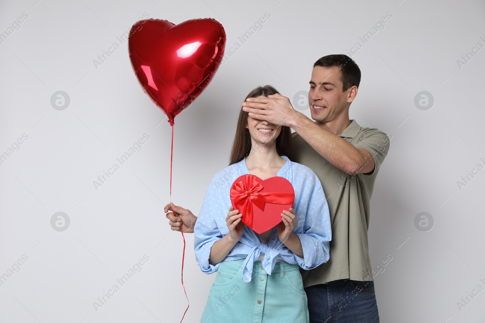 Photo of Lovely man surprising his girlfriend with Valentine's day gift and heart shaped balloon on light background