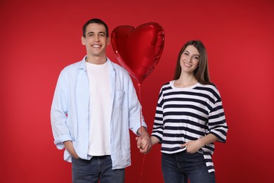 Photo of Lovely couple with heart shaped balloon on red background. Valentine's day celebration