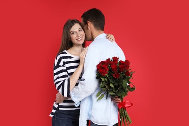 Photo of Lovely man hiding bouquet of roses for his beloved woman on red background. Valentine's day celebration