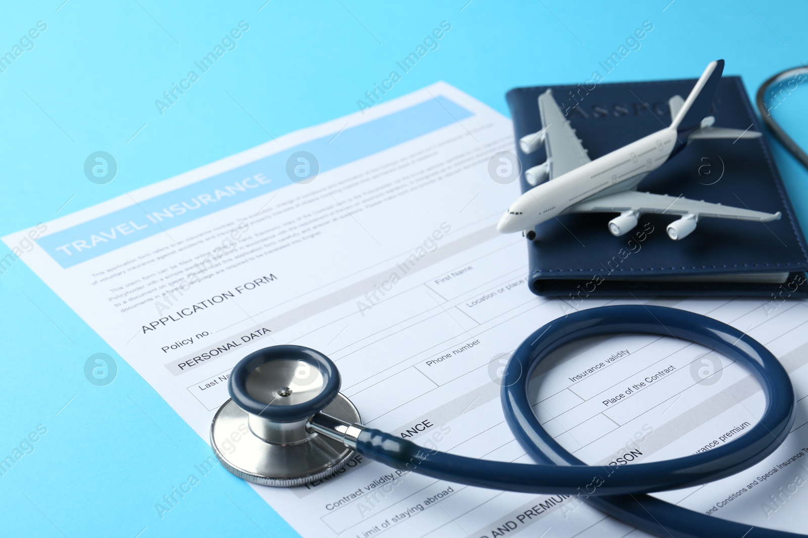 Photo of Medical tourism. Travel insurance application form, stethoscope, passport and plane model on light blue background, closeup