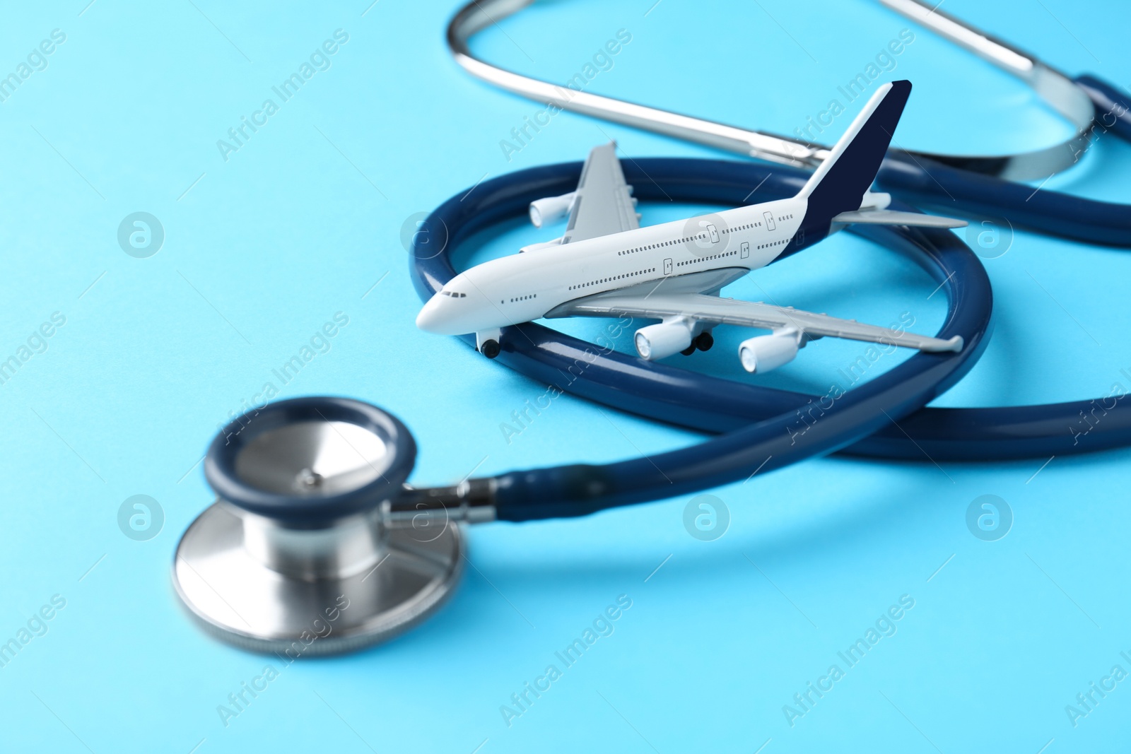 Photo of Medical tourism. Stethoscope and plane model on light blue background, closeup