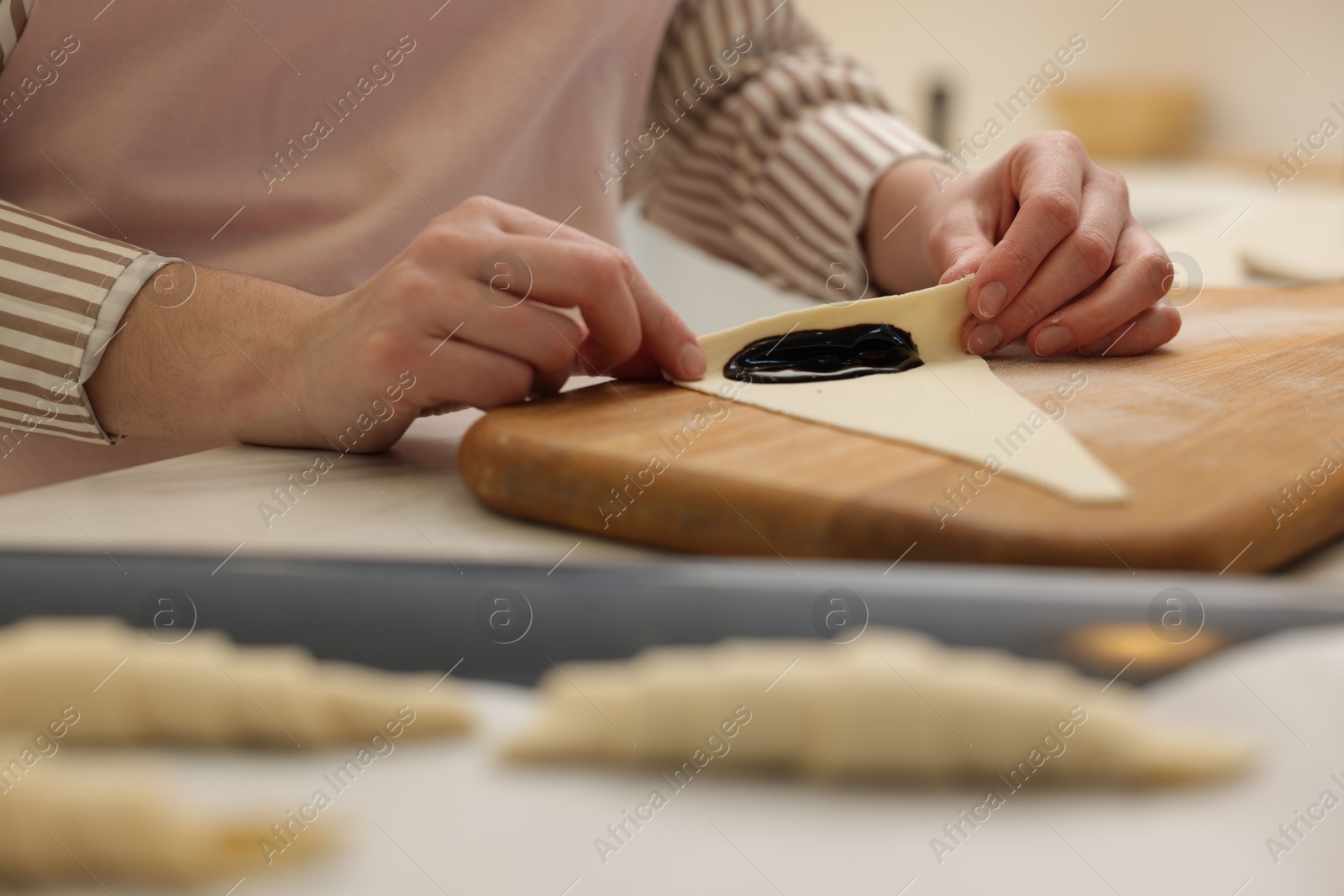 Photo of Woman rolling croissant with jam from fresh dough at table, closeup