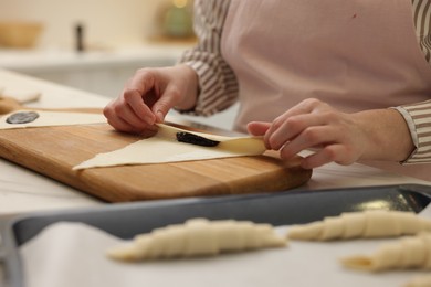 Photo of Woman rolling croissant with jam from fresh dough at table, closeup