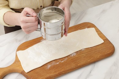 Woman sieving flour onto dough at white marble table, closeup. Making croissants