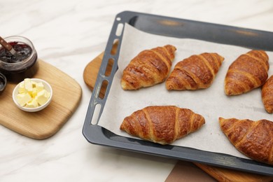 Photo of Freshly baked croissants, butter and jam on white marble table, above view