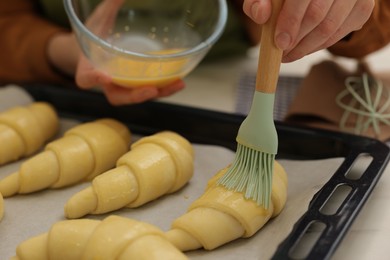 Woman brushing egg wash onto raw croissants at white table, closeup