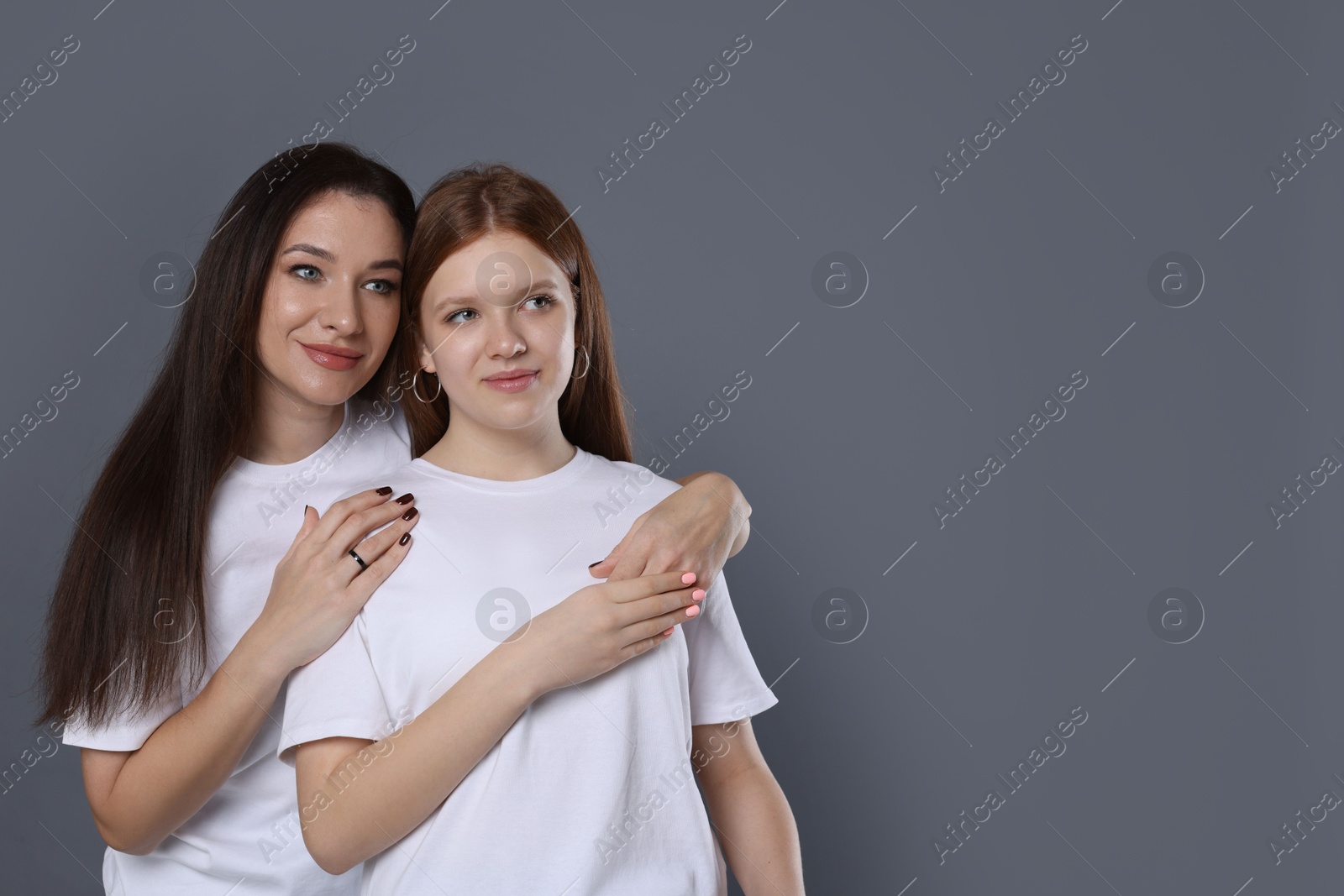 Photo of Family portrait of beautiful mother with teenage daughter on grey background, space for text