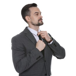 Photo of Confident man in classic suit straightening tie on white background