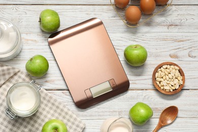 Electronic kitchen scale and products on white wooden table, flat lay