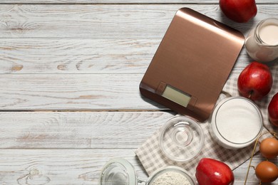 Photo of Electronic kitchen scale and products on white wooden table, flat lay. Space for text