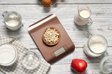 Photo of Electronic kitchen scale and products on white wooden table, flat lay