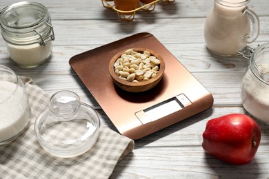 Electronic kitchen scale and products on white wooden table, closeup