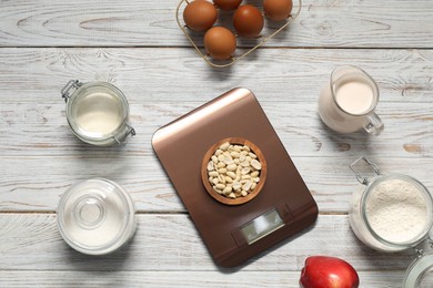 Electronic kitchen scale and products on white wooden table, flat lay