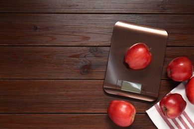 Electronic kitchen scale and apples on wooden table, flat lay. Space for text