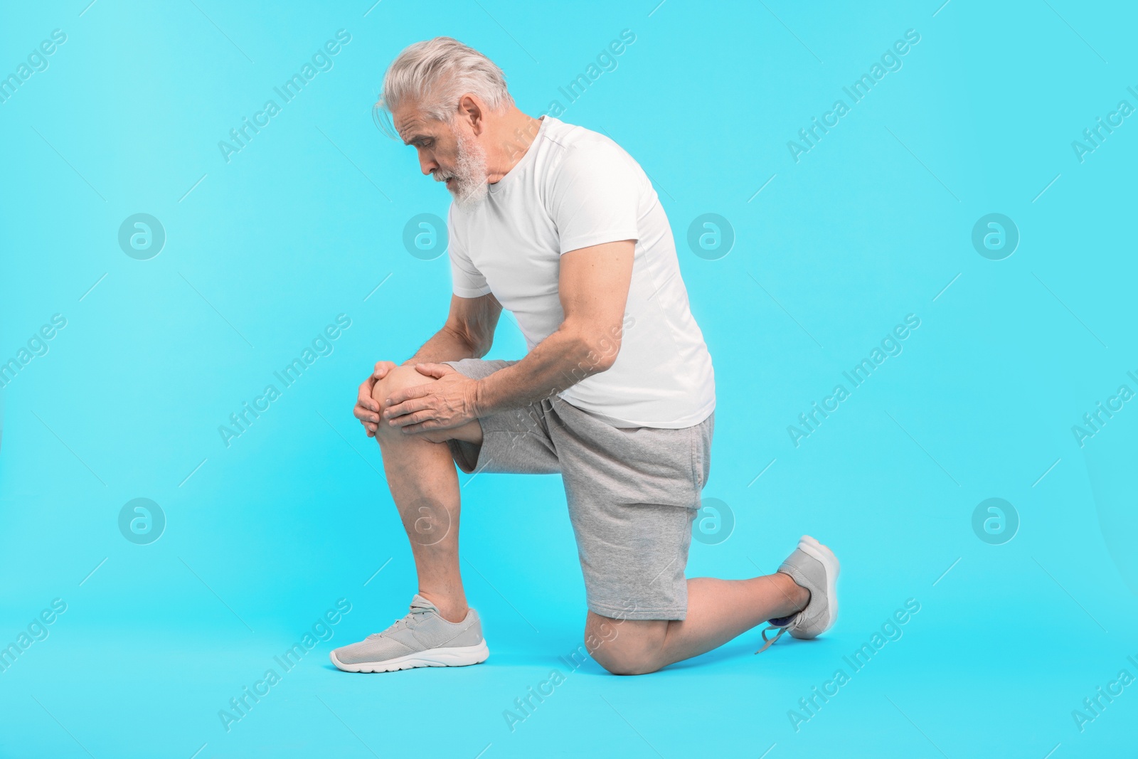 Photo of Senior man suffering from pain in his knee on light blue background