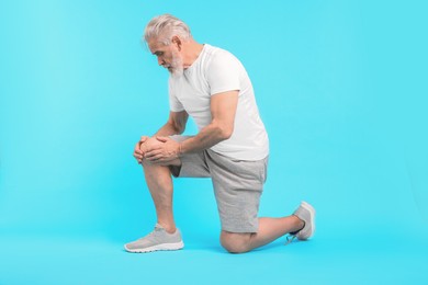 Photo of Senior man suffering from pain in his knee on light blue background