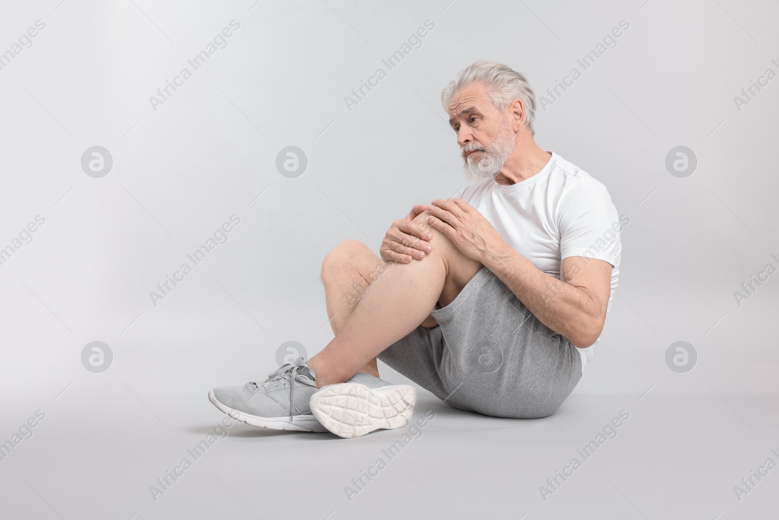 Photo of Senior man suffering from pain in his knee on light background. Space for text