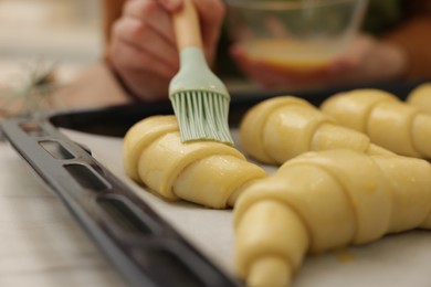 Woman brushing egg wash onto raw croissants at white table, selective focus