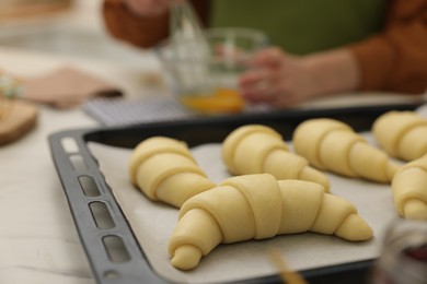 Photo of Woman whisking egg wash near raw croissants at white table indoors, selective focus