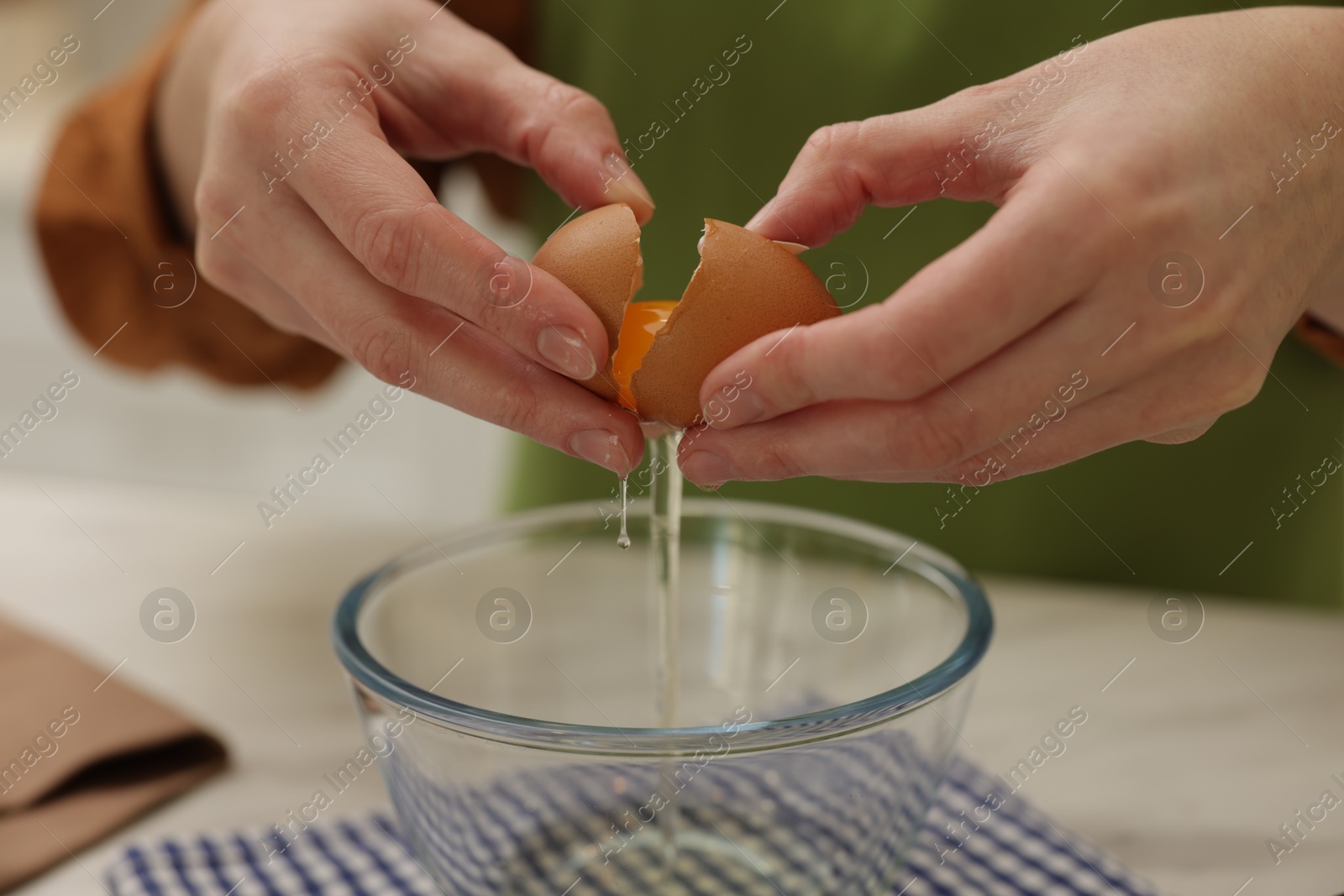 Photo of Woman breaking egg into bowl at white table, closeup