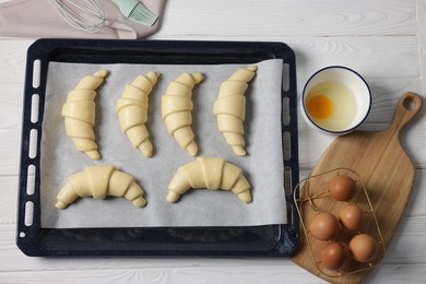 Raw croissants and eggs on white wooden table, flat lay