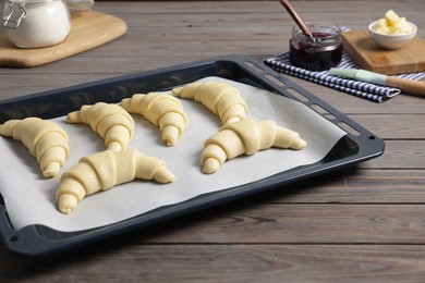 Raw croissants, ingredients and kitchenware on wooden table, closeup