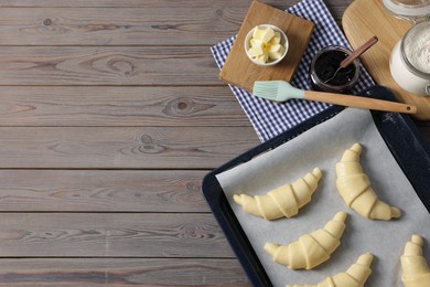 Raw croissants, ingredients and kitchenware on wooden table, flat lay. Space for text