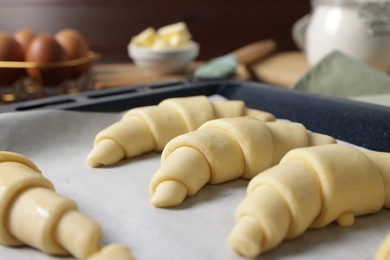 Fresh raw croissants on baking sheet, closeup